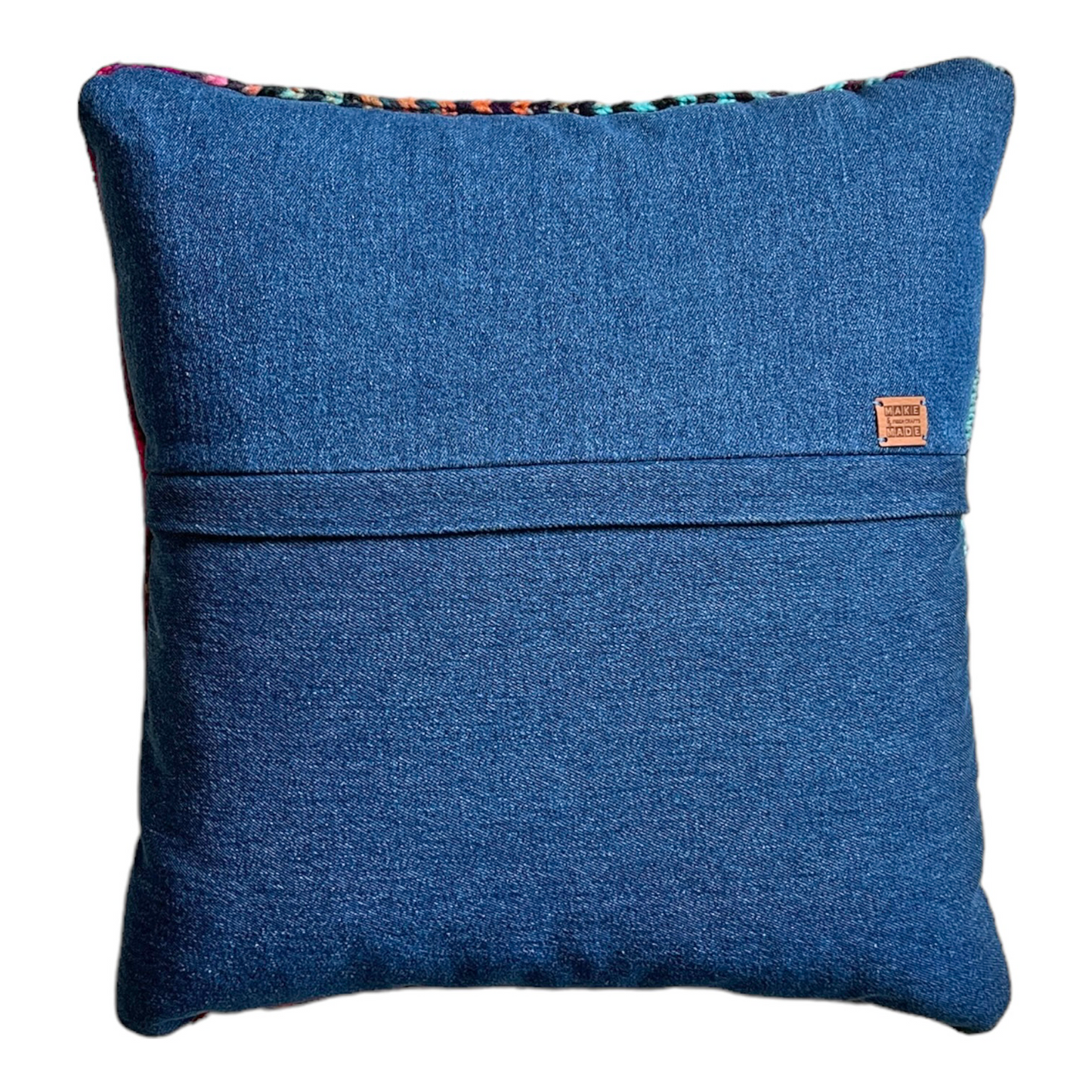The back side of this pillow is a blue cotton denim. A hidden zipper runs horizontally through the middle of the pillow and includes a leather Make & Made Fiber Crafts label.