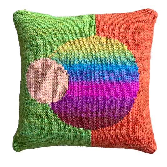The hand-knit side of this pillow features a split background of bright lime (left) and orange (right), punctuated by a large multicolored, striped sphere in the center and a smaller peach sphere, off-centered.