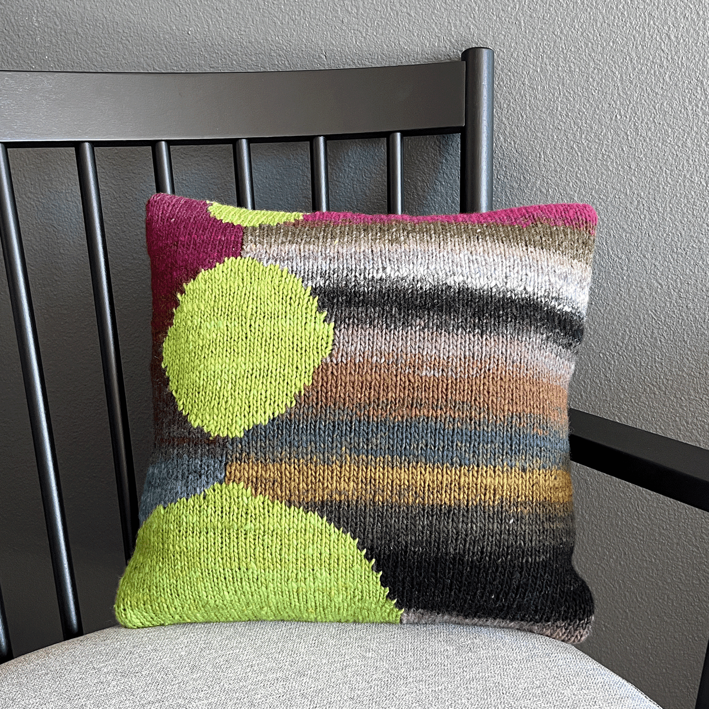 This 100% wool, hand-knit decorative throw pillow features bright chartreuse spheres against a striped background of saturated neutrals.