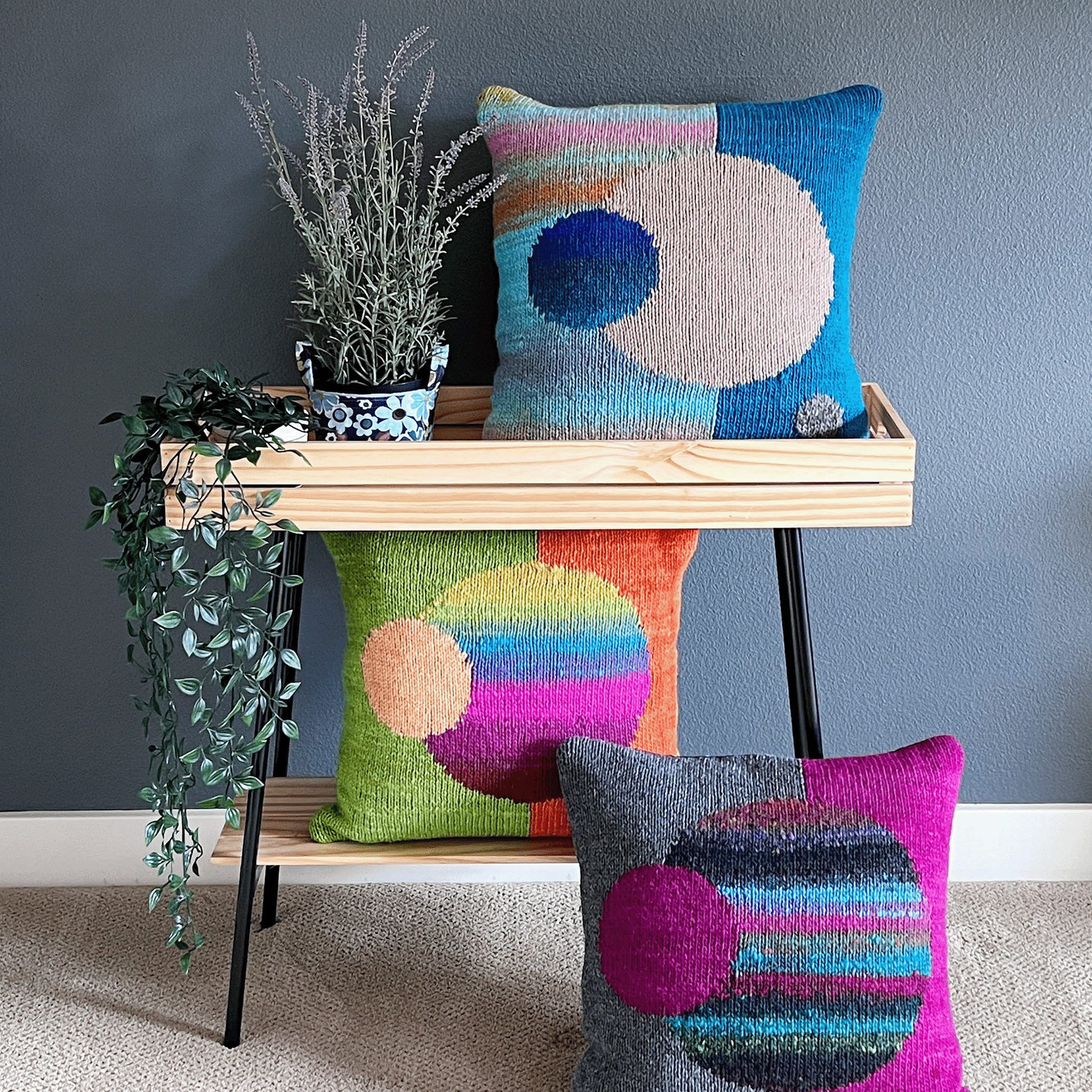 Vibrant, decorative throw pillows from the Celestial Series, hand-knit by Susan in 100% wool, are displayed against a charcoal background.