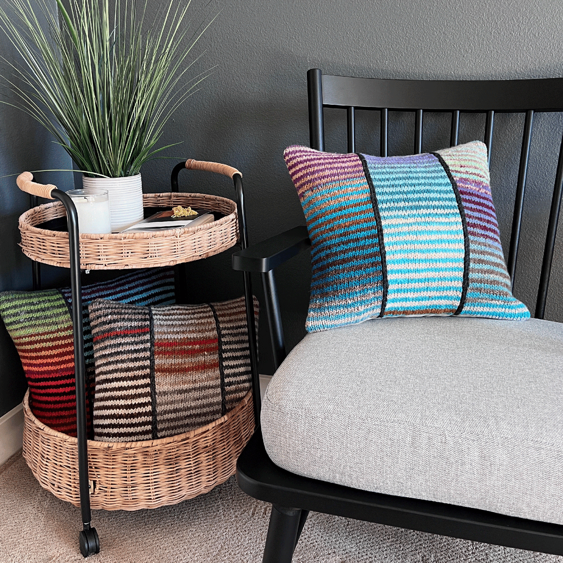Three decorative throw pillows, hand-knit by Susan in 100% wool, display bold stripes in vibrant hues against a black shaker-style chair.