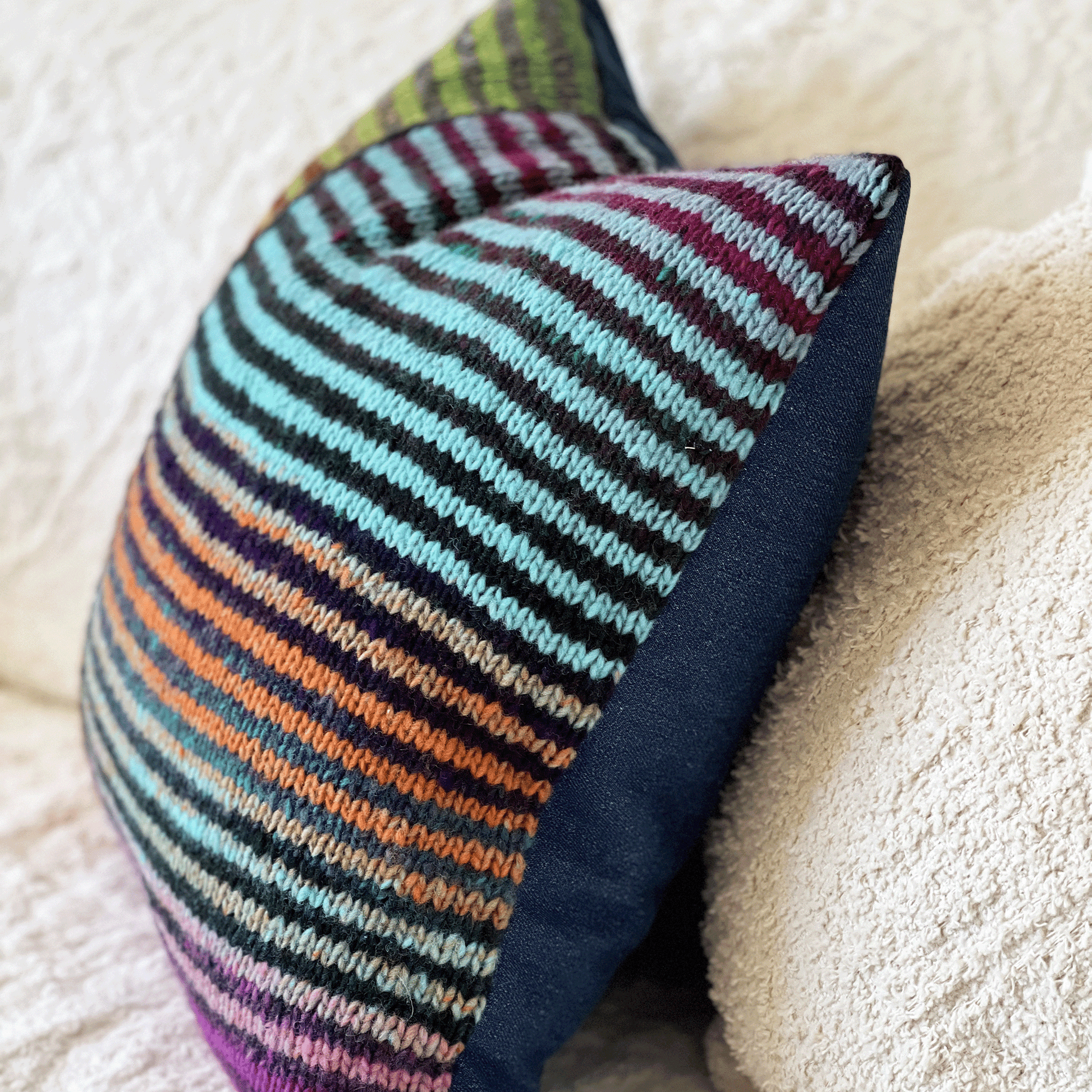 This 100% wool, hand-knit decorative throw pillow with variegated stripes pops against an off-white, shabby chic, boho-style couch.