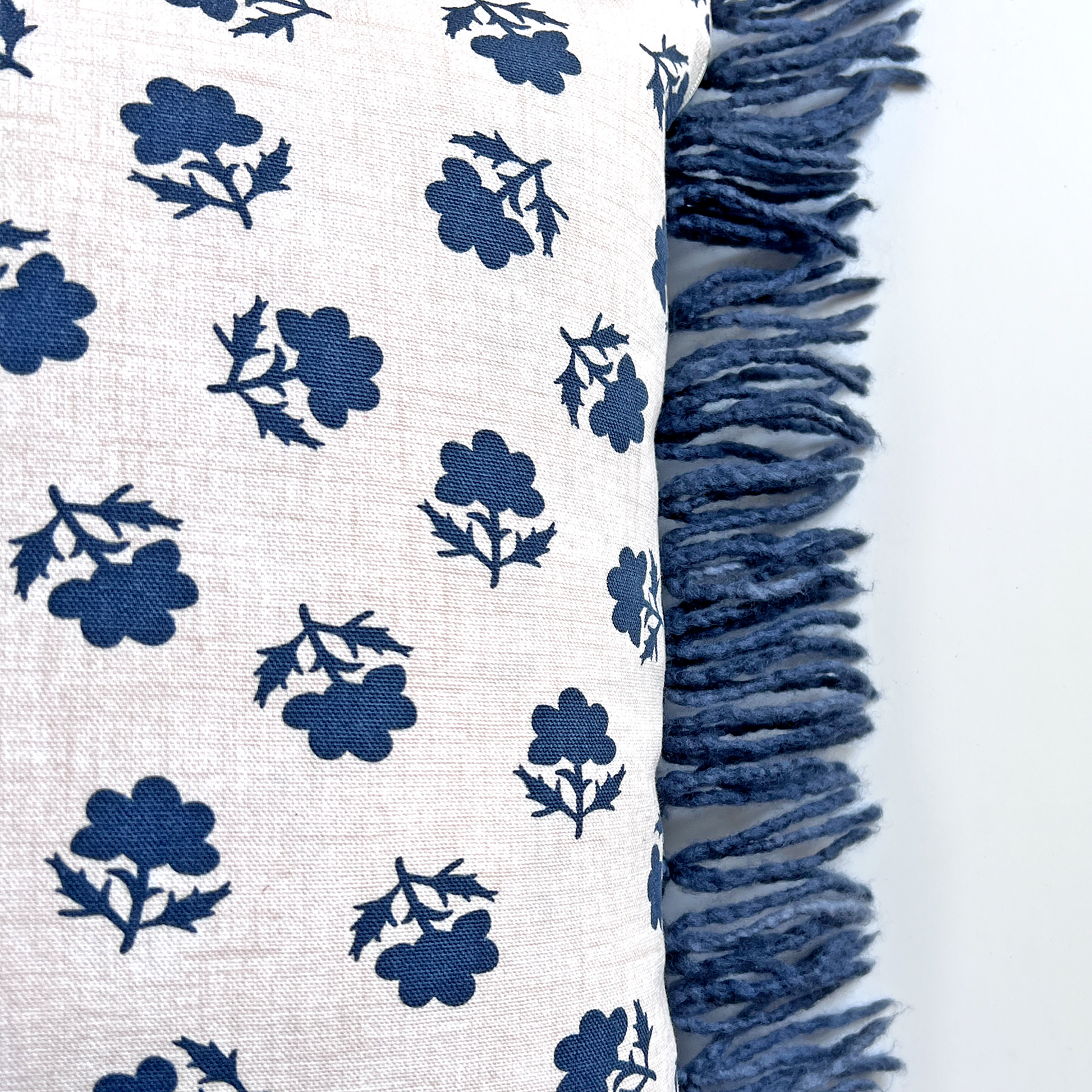 The back of this uniquely fringed pillow is a natural cotton canvas with a medium-sized navy floral print.