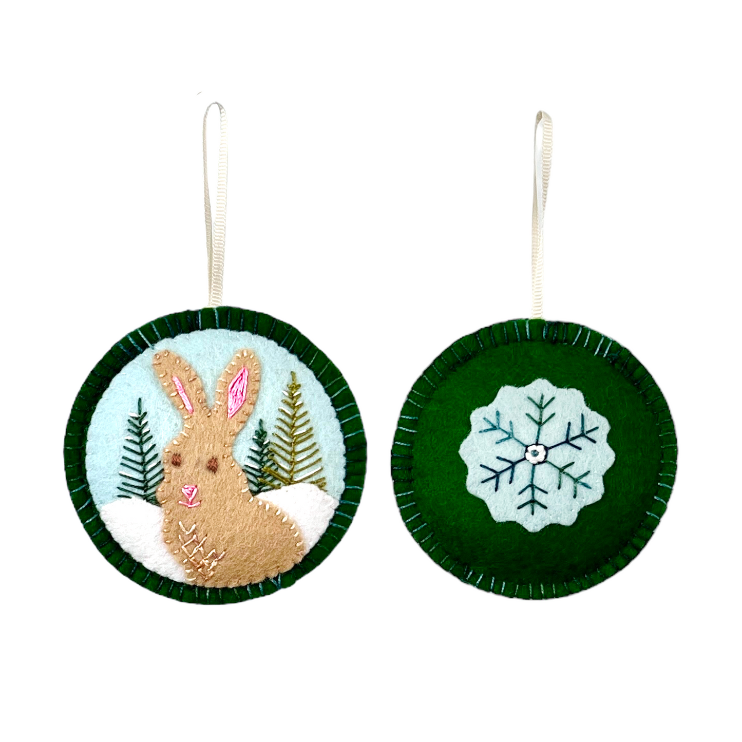 A plump, tan bunny with a satiny pink nose is the star of this Winter Animal wool felt ornament. It sits in the snow against a pale blue sky in front of three embroidered fir trees. On the reverse, an embellished snowflake brings color to a forest green felt ornament back.