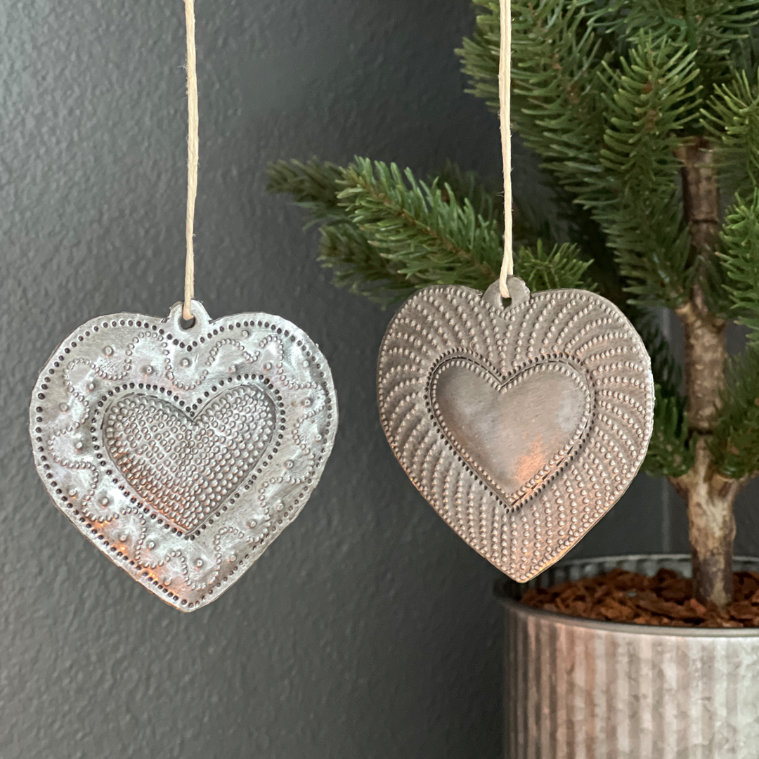Haitian Heart ornaments cut from recycled steel drums in two styles hang side-by-side in front of a miniature Christmas tree.