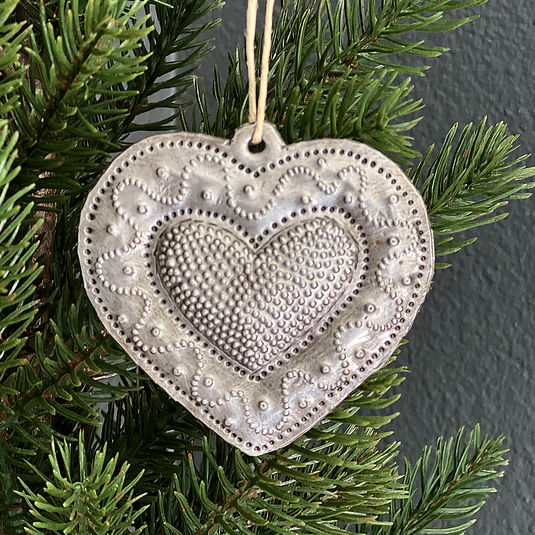 The "squiggle" style ornament features an inner heart filled with dots, surrounded by a smooth outer heart embellished with a squiggly row of dots.. The loop for hanging is made of twine.