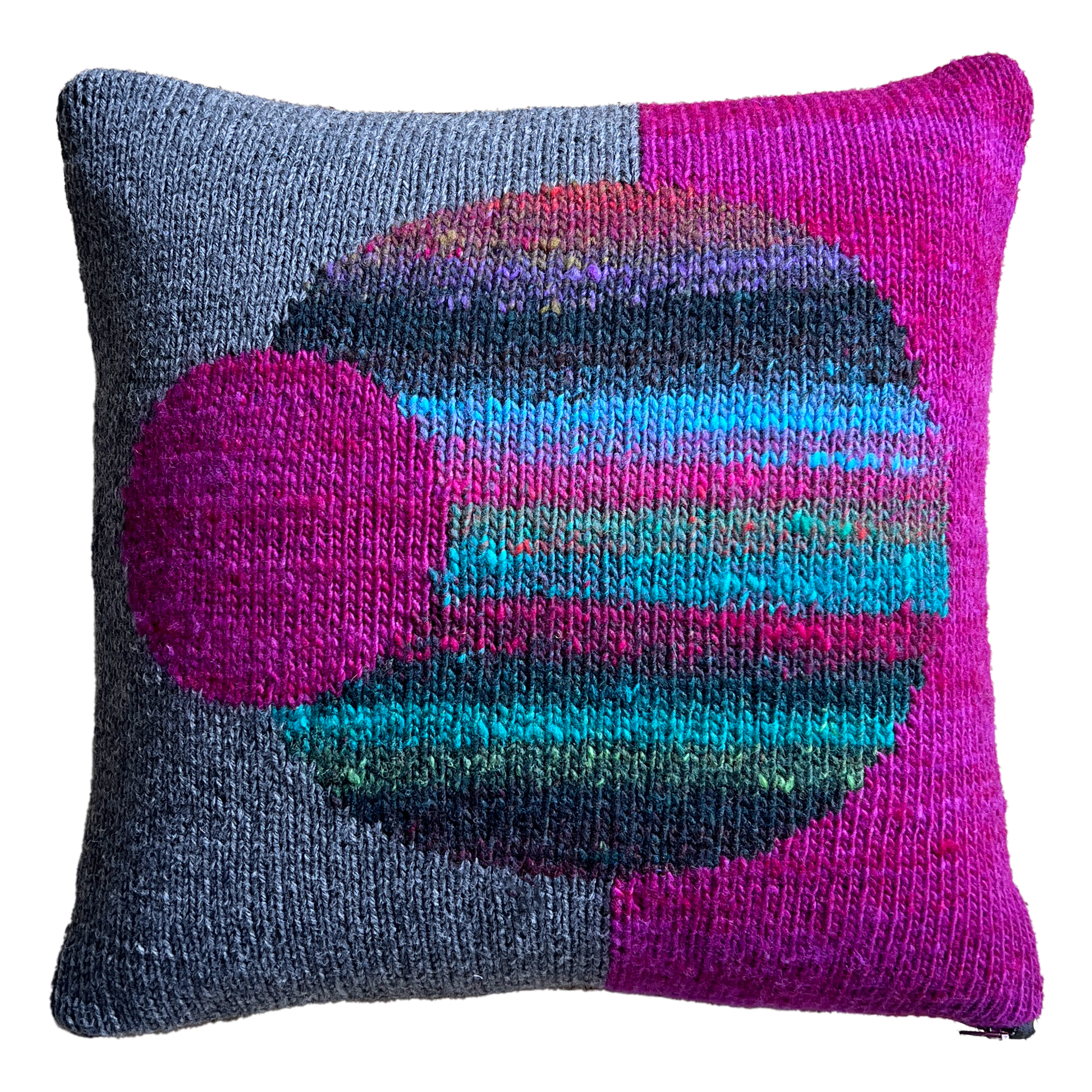 The hand-knit side of this pillow features a split background of charcoal gray (left) and magenta (right), punctuated by a large multicolored, striped sphere in the center and a smaller magenta sphere, off-centered.