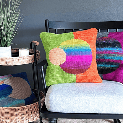 Vibrant, decorative throw pillows from the Celestial Series, hand-knit by Susan in 100% wool, are displayed against a black shaker chair.