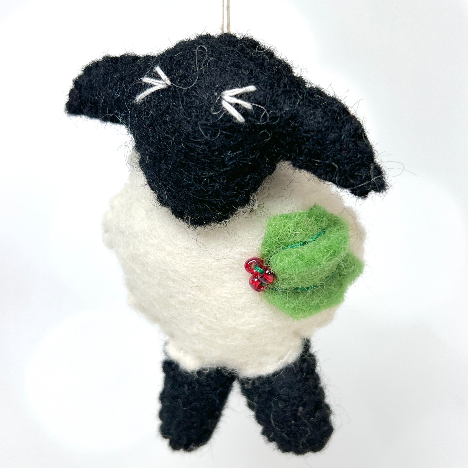 A plump wooly white body separates this sweet sheep's black head from his two black legs. A sprig of holly decorates his wooly chest.