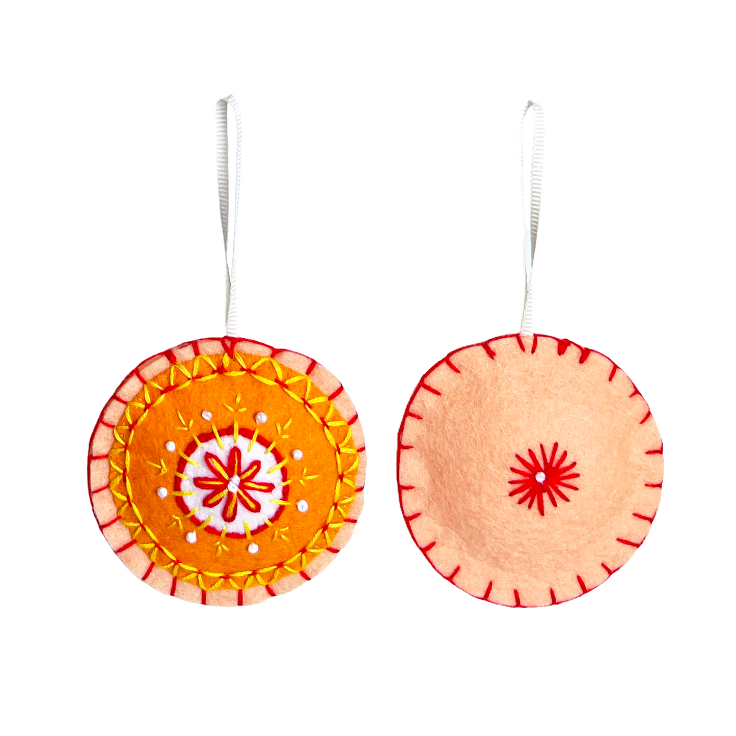 This Mini Mandala ornament features concentric circles of white, orange, and peach felt with a matching peach felt back. Both sides are embroidered using orange, yellow, and white threads in a symmetrical, mandala-inspired design.