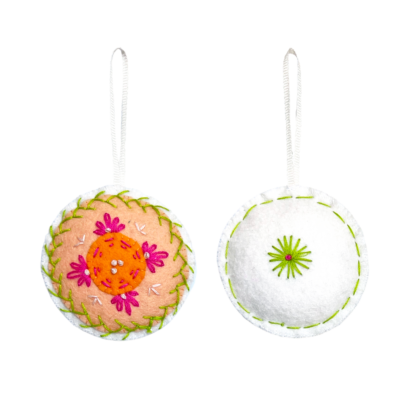 This Mini Mandala ornament features concentric circles of orange, peach, and white felt with a matching white felt back. Both sides are embroidered using lime green, dusty rose, and white threads in a symmetrical, mandala-inspired design.