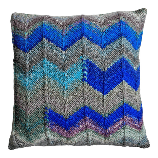 This decorative throw pillow is hand-knit with 100% wool yarn in chevron stripes of blue, gray, hunter green, and turquoise.