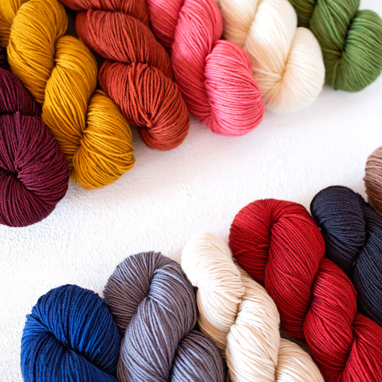 Several skeins of Urth's Harvest DK Yarn against a white background in multiple colors